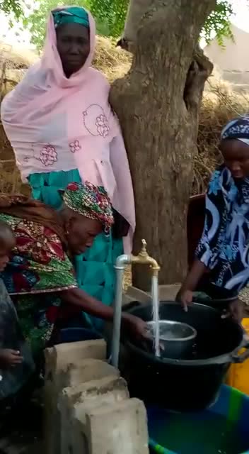 Women and a small child fill basins at a village water point in Mali funded by the Foundation