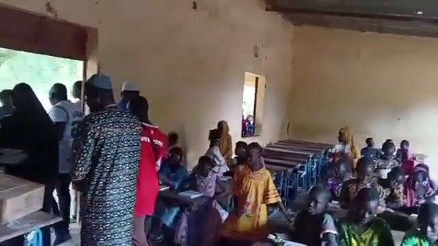 Children at their desks in a rural classroom in Mali as volunteers hand out school supplies